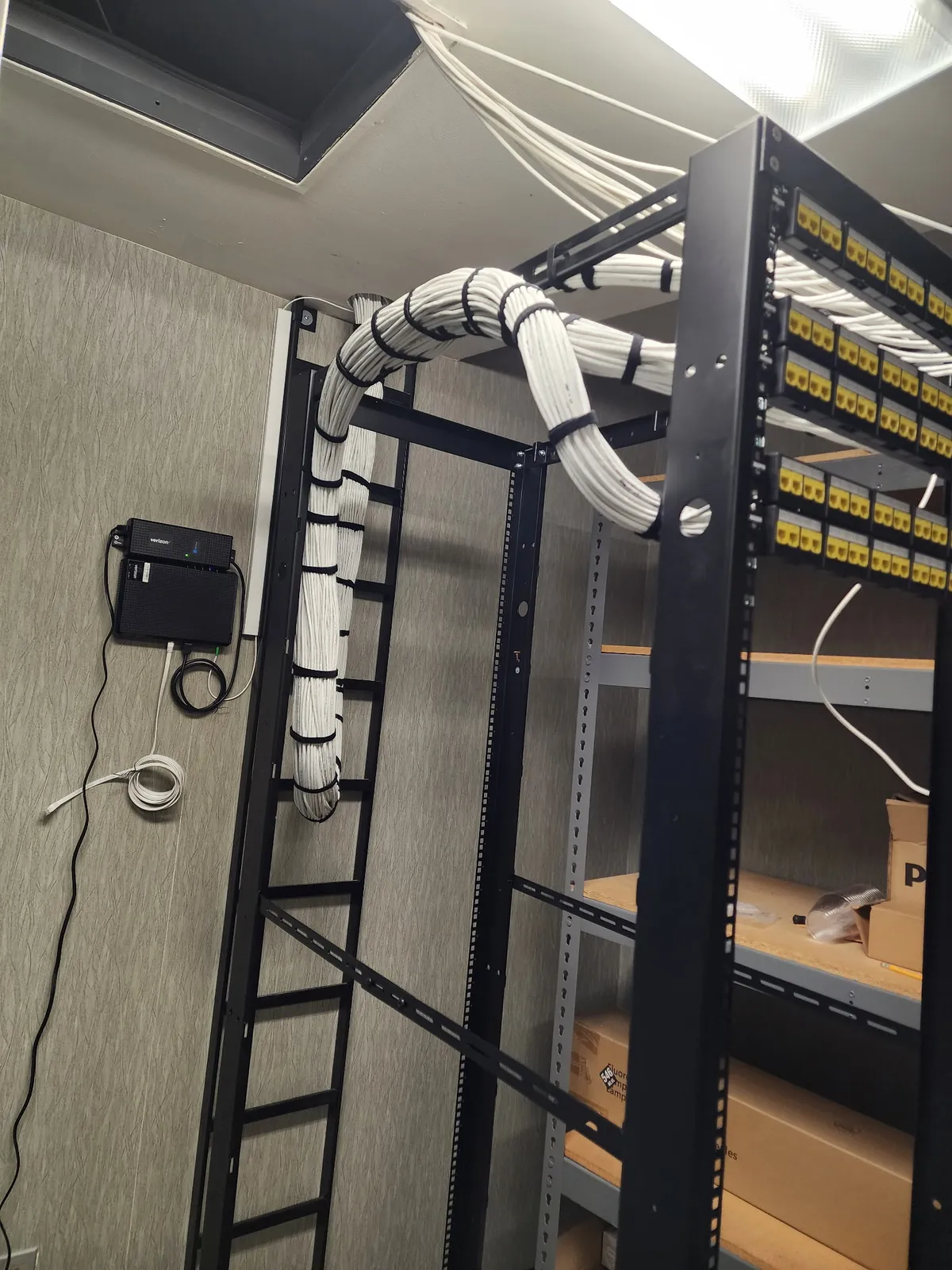 MDF closet with cable waterfall to yellow patch panels and wall-mounted Verizon ONT