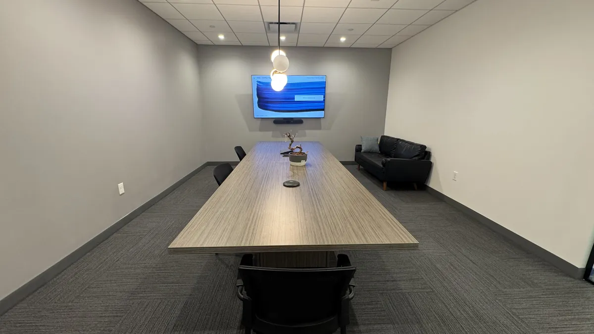 Conference room with wall-mounted display, camera bar, pendant light, and leather seating
