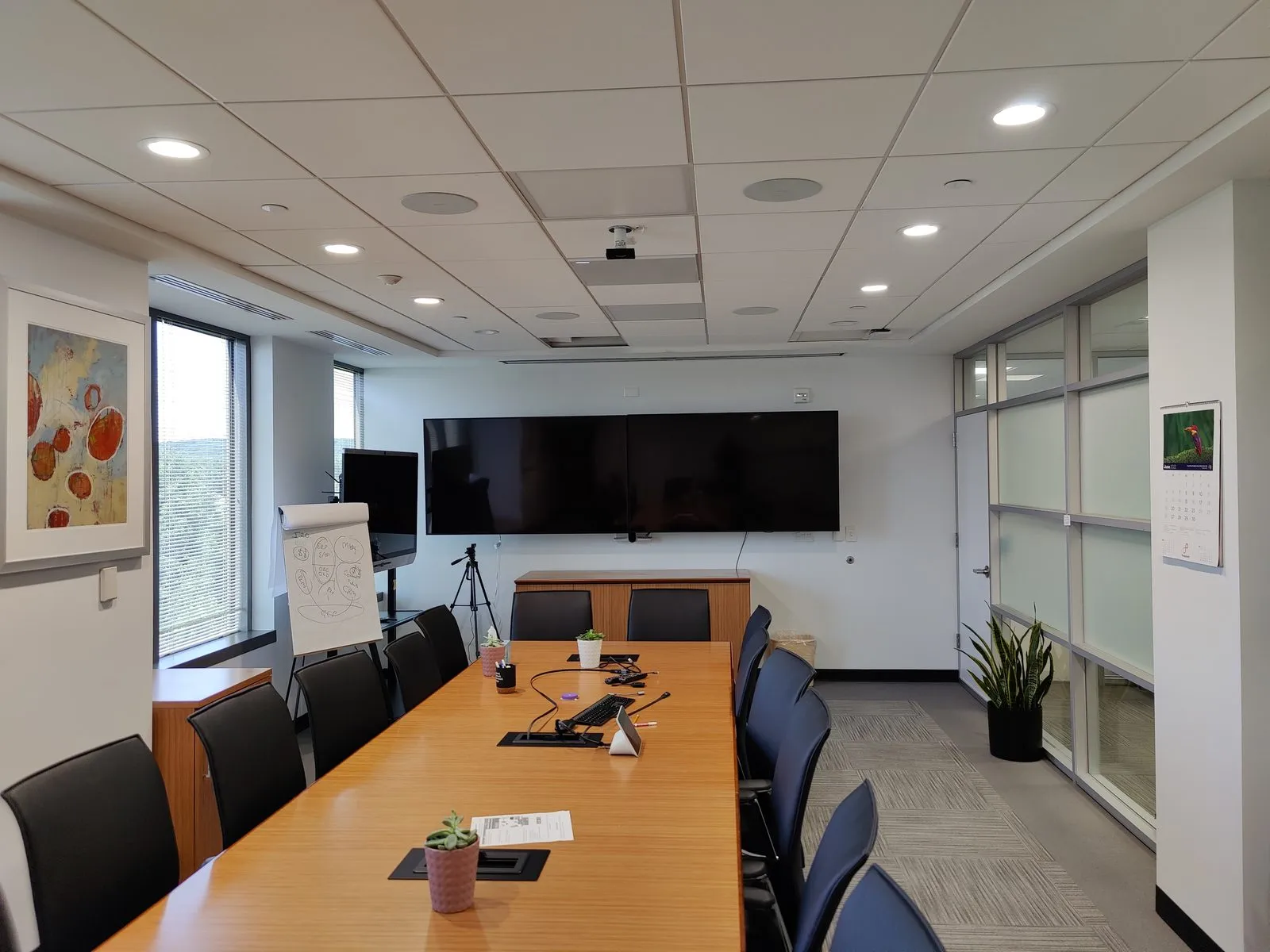 Boardroom with dual wall-mounted displays, ceiling speakers, and projector